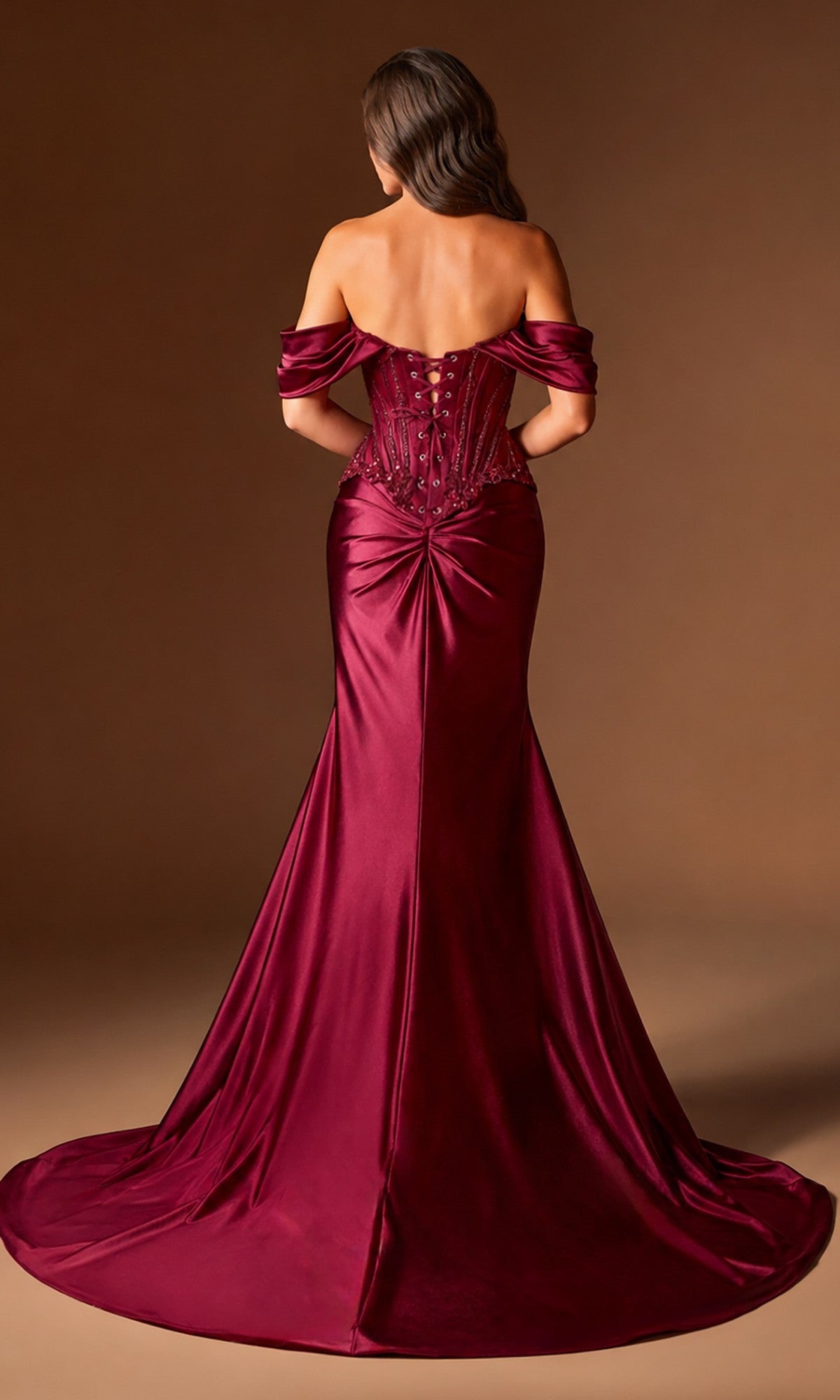 A woman wears the Ladivine CD656 long prom dress, featuring an off-the-shoulder satin design with a fitted bodice, lace-up back, gathered lower back detail, and floor-length burgundy skirt against a brown background.
